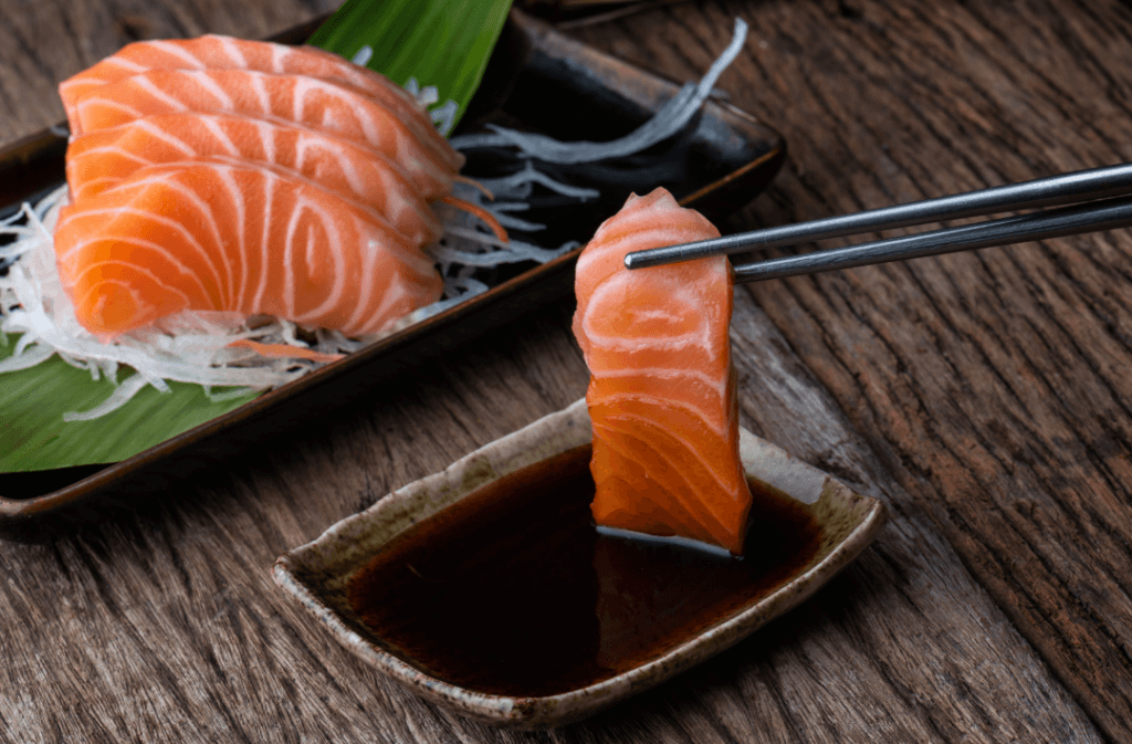 Mulher segurando sashimi de salmão no molho shoyu